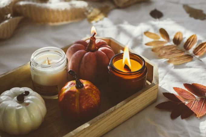 dřevěný podnos s atmosférickými svíčkami a podzimním podzimním listím na bílé posteli