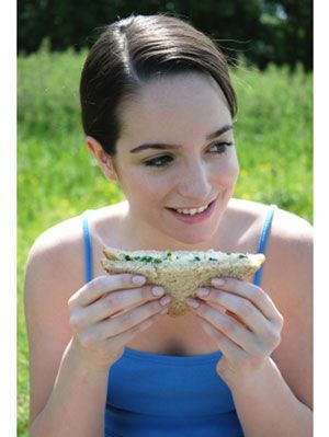 lány ül a fűben, eszik egy szendvicset