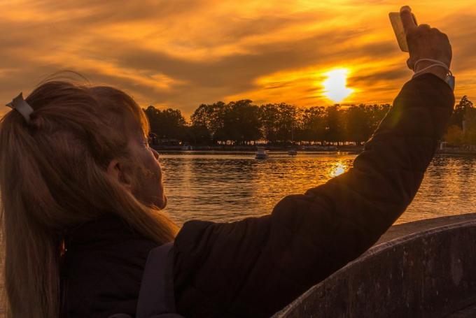 suaugusi moteris vakare fotografuojasi su ežeru už nugaros
