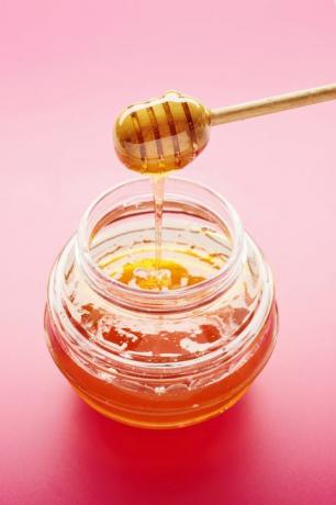 Cazo de miel con miel líquida en tarro sobre fondo rosa