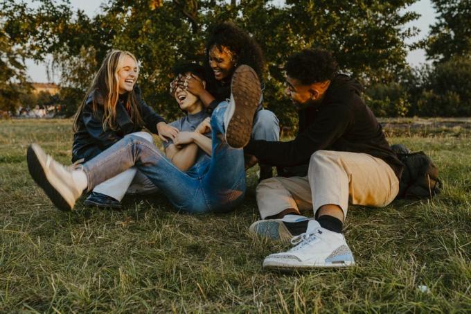 joyeux amis masculins et féminins s'amusant en jouant dans le parc au coucher du soleil