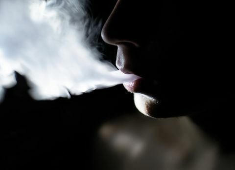 Orezaný obrázok muža bez košele fajčiaceho v tme
