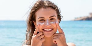 opalona kobieta chroni twarz kremem do opalania przed poparzeniem słonecznym na plaży