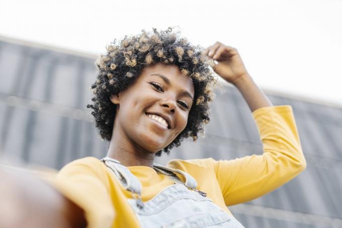 donna afro spensierata con le cuffie che guarda l'obbiettivo e sorride mentre si fa un selfie all'aperto