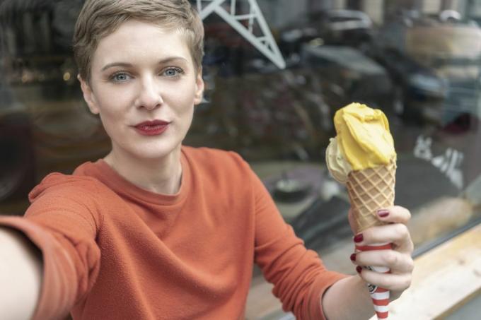 sieviete uzņem selfiju ar saldējumu veikala priekšā