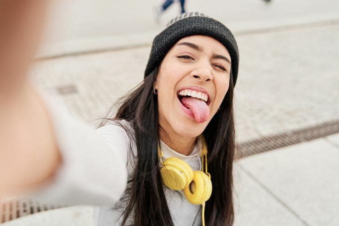 latina tar en selfie med smarttelefonen som stikker ut tungen og blunker latinamerikansk kvinne som lager et morsomt ansikt mens hun tar en selfie